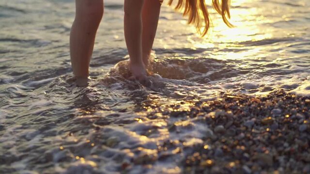 at sunset little girl walks along seashore and throws stones into water.