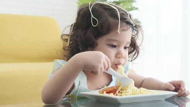 Little girl eating and making total mess of spaghetti on her head.