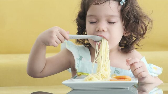Happy little girl eat delicious spaghetti and tomatoes.