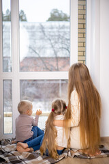 A beautiful and happy young mother and her children son and daughter at home by the window. Comfort. Warm tones.