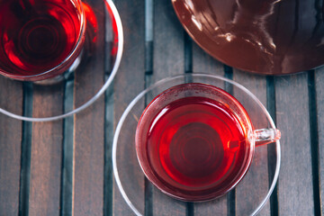 Glass cup of hot red hibiscus tea and and old retro teapot on a wooden tray at terrace. Close up. Top view