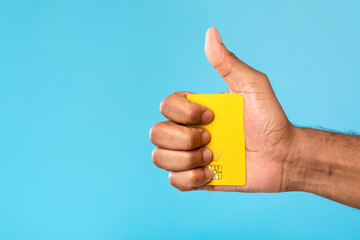 Cropped view of millennial black man holding credit card and gesturing thumb up on blue studio background, empty space