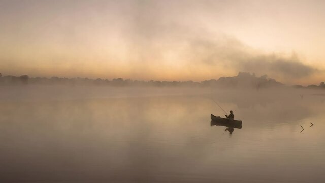 Aerial static shot of a man fishing by himself before the sunrise in a lake at Imire, Zimbabwe