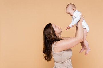 Side view of smiling woman holding baby daughter isolated on beige.
