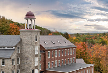 Beautiful sky and colorful autumn scene in historic town of Harrisville, New Hampshire. Old bell tower and preserved textile mill buildings built of granite and brick in 19th century. - obrazy, fototapety, plakaty