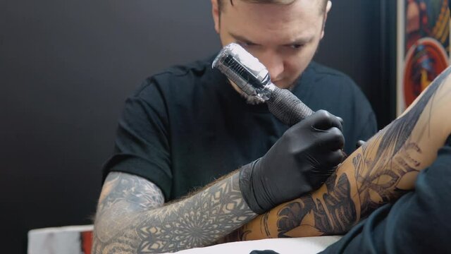 A tattoo artist with a tattooed arm makes a full arm tattoo to his client. Artistic permanent image on the human body