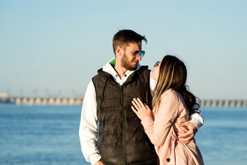 Fototapeta premium Happy young lovers stand enjoy vacation by sea beach. Lovely hipster couple hugging and having fun together outdoors. Concept of youth, love and lifestyle.