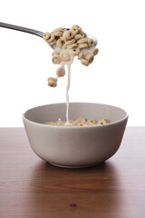 Photo of a spoon pouring lopp oat cereals into a white bowl full of cereals with milk