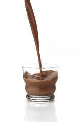 Pouring chocolate drink into a transparent glass isolated in a white background with reflection