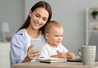 Young Mother Messaging On Smartphone While Spending Time With Baby At Home