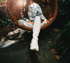 A young girl sits in a cocoon hanging chair. Brunette woman in the indoor urban jungle