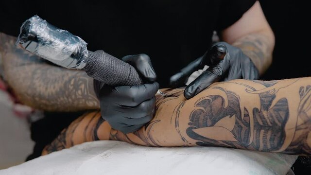 The process of tattooing with a tattoo machine with a woman's face on a man's hand in a tattoo parlor