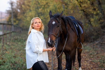 Fototapeta premium beautiful caucasian girl in a white shirt with a horse in the forest at sunset