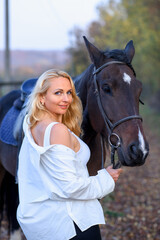 Fototapeta premium beautiful caucasian girl in a white shirt with a horse in the forest at sunset
