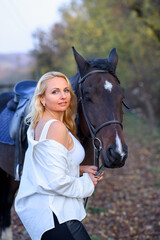 Obraz premium beautiful caucasian girl in a white shirt with a horse in the forest at sunset