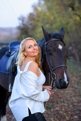 Obraz premium beautiful caucasian girl in a white shirt with a horse in the forest at sunset