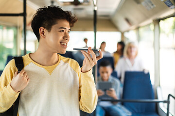 Fototapeta na wymiar Smiling Asian guy taking bus, talking on cellphone