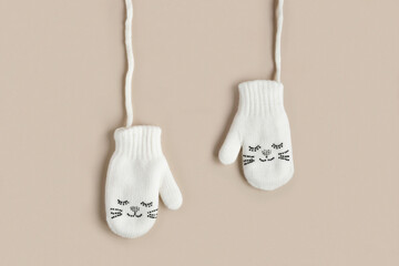 White knitted baby mittens isolated on a natural beige background, top view. Winter kids clothes....