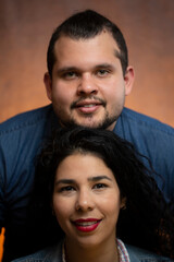 Young couple poses for a studio portrait with the gentleman above the lady, selective focus on the lady. Orange color background.