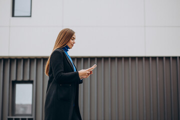 Young woman in black coat using phone