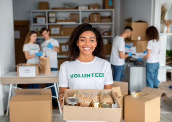 Young black female volunteer holding food donation box and smiling to camera while posing to camera...