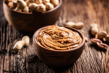 Peanut butter in wooden bowl and peanuts on rustic oak table