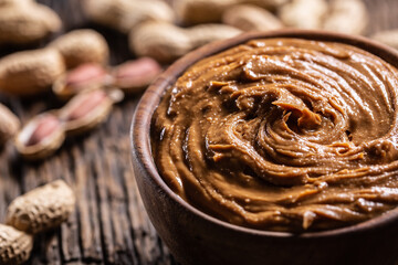 Peanut butter in wooden bowl and peanuts on rustic oak table