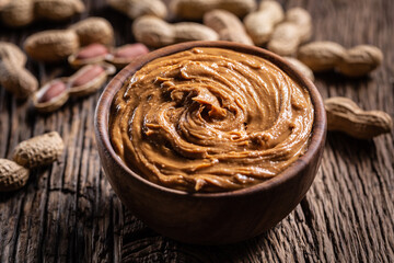 Peanut butter in wooden bowl and peanuts on rustic oak table