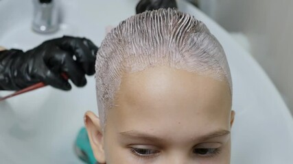 a hairdresser stylist in gloves carefully dyes the hair of a teenage girl with a flat rare comb. The client yawns with boredom while dyeing his hair