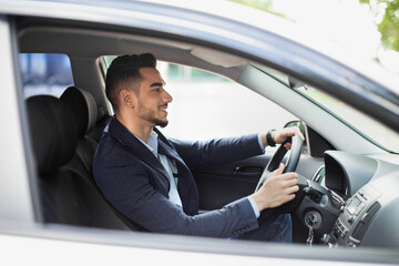 Cheerful middle eastern manager driving car, side view