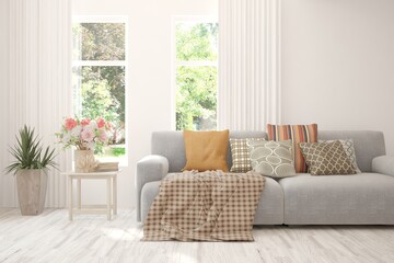 Fototapeta premium White living room with sofa and summer landscape in window. Scandinavian interior design. 3D illustration