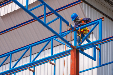 Low angle view of construction worker with safety equipment is welding metal roof warehouse building structure in construction site