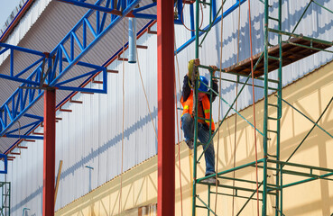 Fototapeta premium Construction worker with safety workwear climbing on scaffolding for working on roof warehouse structure in construction site