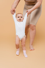 Plus size woman holding hands of baby daughter while walking on beige background.