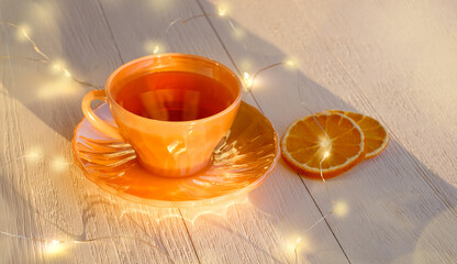 Cup of tea and slice of dried orange, christmas garlands on white wooden background. New Year morning tea