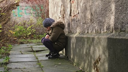 Sad Depressed Caucasian Girl Crying and Sitting Huddled Alone By the Wall Outdoors Holding Her...