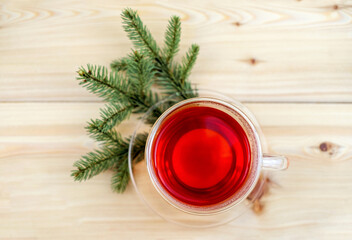 Glass cup of tea and pine branches on wooden background, top view