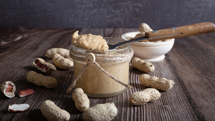 Peanut paste in a jar and nut kernels on a wooden background