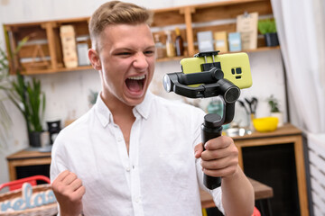 Young handsome guy filming a video blog on a mobile device using an electronic image stabilizer in...