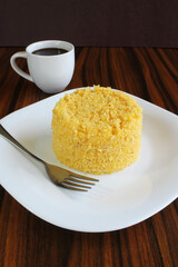 Corn couscous in a white plate with a black coffee on the background. Brazilian food.
