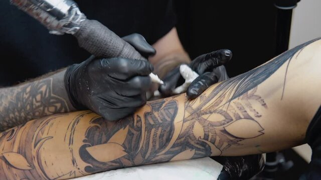 The process of tattooing with a tattoo machine with a woman's face on a man's hand in a tattoo parlor