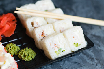 Sushi rolls with cheese, shrimp, chicken and cucumber in plastic packaging for takeaway on a dark background