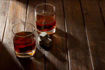 Transparent glass with whiskey on a dark wooden background with bright rays of light. Whiskey stones in the grocery