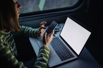 A woman uses gadgets with a smartphone and a laptop while traveling by train. Freelancer works at...