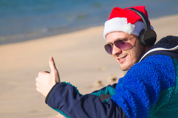 smiling man with christmas santa hat and headphones on the beach celebrating christmas