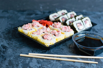 Delicious sushi with soy sauce, fish, cheese, caviar, wasabi and ginger in plastic packaging for takeaway on a dark background