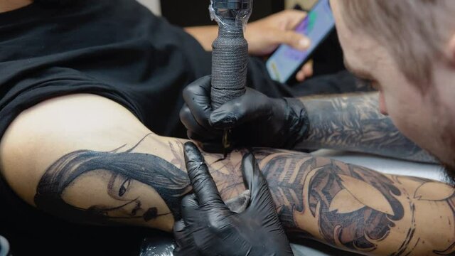 The tattoo artist draws small details in the picture. Tattoo with a woman's face on a man's arm