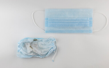 A used crumpled medical mask lies on a white background. There is a  of new mask nearby.