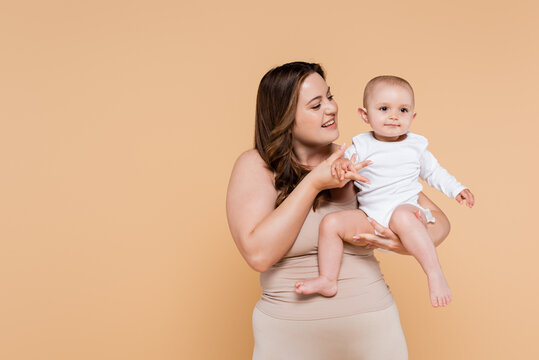 Happy Plus Size Woman Holding Hand Of Child Isolated On Beige.