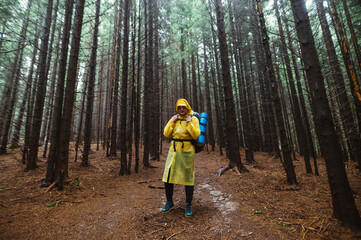 Naklejka premium Young male hiker in a raincoat stands in the woods and looks away with a serious face on a background of beautiful view